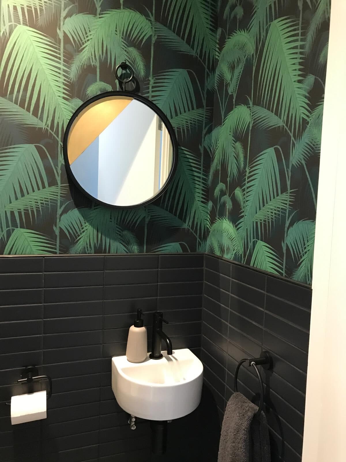 Cloakroom with palm-print wallpaper over black metro tiles